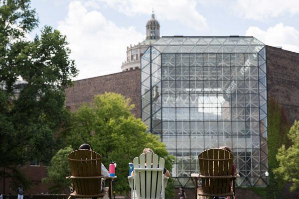 A young adult poses for a photo in front of the University of Rochester's Rush Rhees Library.